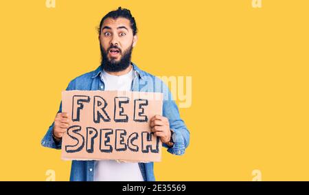Young arab man holding free speech banner scared and amazed with open mouth for surprise, disbelief face Stock Photo