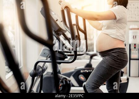 Active pregnant woman exercise in fitness center at yoga room. The young expecting mother holding baby in pregnant belly. Maternity prenatal care and Stock Photo