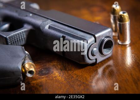 A black semi-automatic pistol and ammunition on a wooden table. Stock Photo