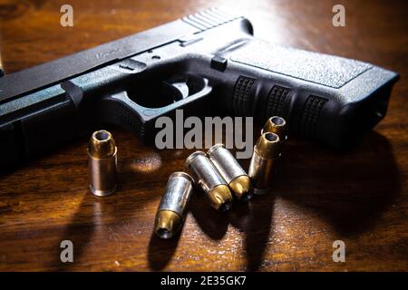 A black semi-automatic pistol and ammunition on a wooden table. Stock Photo