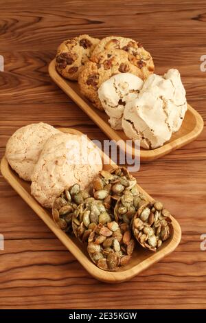 Oatmeal cookies with walnuts and raisins, sugar-coated pumpkin seed cookies,  meringue cookies with hazelnuts, almond cookies in a bamboo plates on a Stock Photo