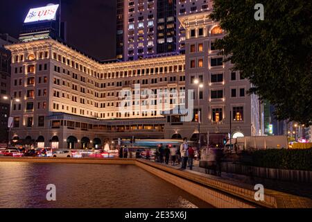 As evening falls over the Peninsula Hotel, the soft glow of city lights reflects off the fountain.capturing the vibrant pulse of Hong Kong's nightlife Stock Photo