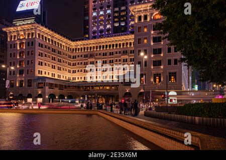 As evening falls over the Peninsula Hotel, the soft glow of city lights reflects off the fountain.capturing the vibrant pulse of Hong Kong's nightlife Stock Photo