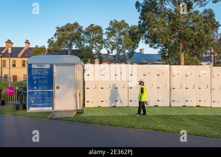 A cleaner wearing a Covid mask stands in front of a disabled access portable toilet and a row of single portable toilets at a Sydney Festival event.