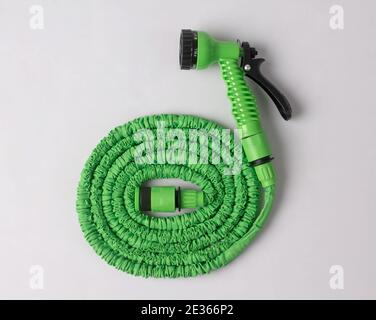 green garden hose coiled with spray nozzle isolated on white background Stock Photo