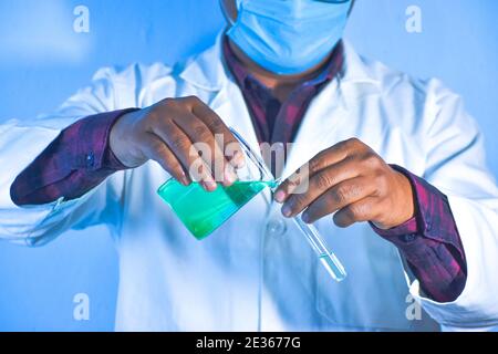 Chemist with chemical solution. Scientist pouring color liquid from beaker into a test tube, closeup. Stock Photo
