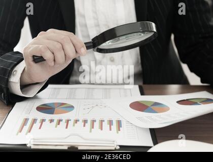 Business Analyst using magnifying to review business graphs. Concept of analyze business growth and market share analysis. Stock Photo