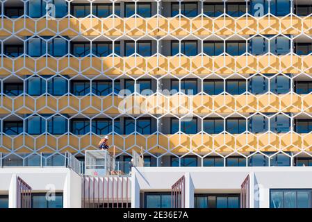 Two construction workers are dwarfed by the size of the building they are working in front of in Granville, western Sydney, New South Wales, Australia Stock Photo