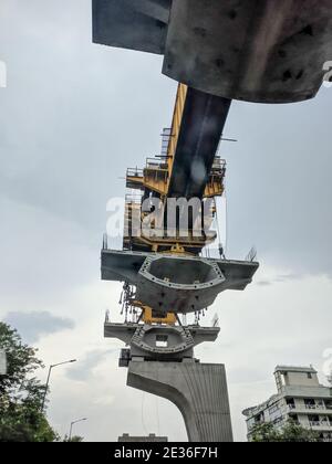 Looking up shot of of construction of metro bridge using modular concrete rings and a crane on a busy street during rains Stock Photo