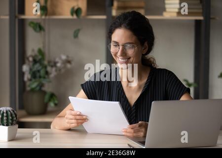 Smiling young woman read documents working on laptop Stock Photo