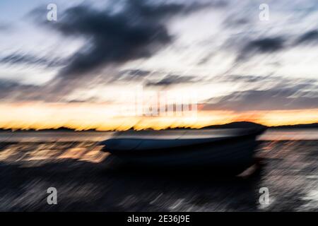 Intentional camera movement blurs in dark morning light impressionist style on beach with dinghy Stock Photo