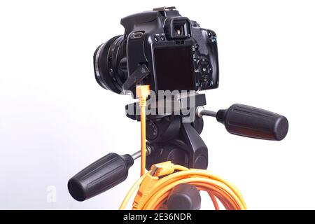 Digital photo camera on black tripod with orange rolled cable isolated on white background. Stock Photo
