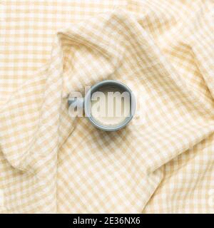 Cup of milk tea on crumpled beige check pattern fabric background. top view Stock Photo