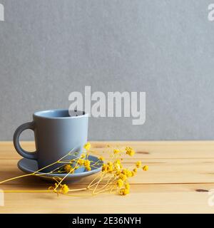 Coffee cup with yellow gypsophila dry flowers on wooden table. gray background Stock Photo