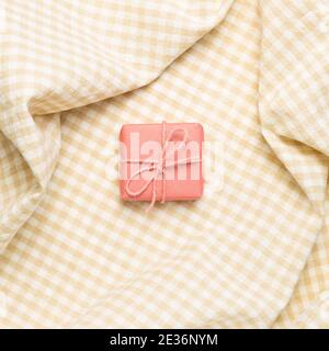 Pink gift box on crumpled beige check pattern fabric background. top view Stock Photo