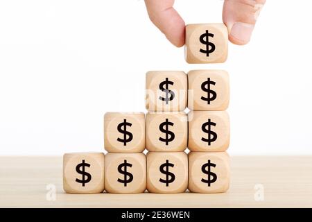 Growth, savings, wealth or richness concept. Hand holding a wooden block and blocks stacked with dollar symbol. Copy space. White background