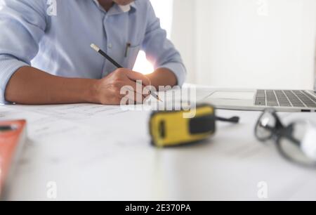 Young engineers or architect holding pen and drawing plan on blueprint in working site. Stock Photo