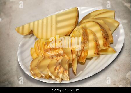 Italian seasoned caciocavallo, slices of typical Apulian cheese in white plate on spotted background, top view Stock Photo