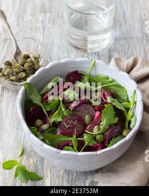 Vegan healthy beetroot salad with baked red onion, capers, watercress, greens and vinaigrette sauce on a wooden table. Delicious homemade food Stock Photo