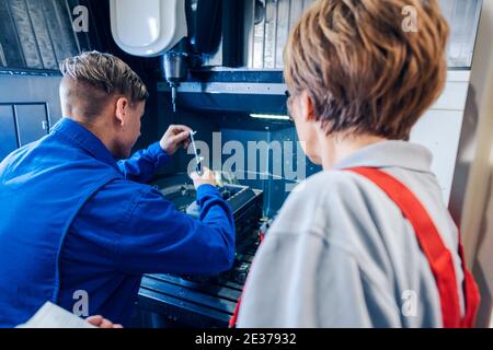 Supervisor watching young worker changing setup of lathe machine Stock Photo