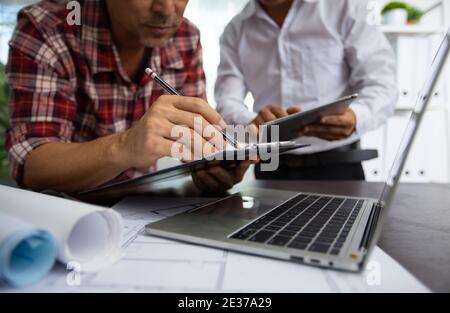 close up hand of engineer explaining project work on tablet and discussing about drawing blueprint as partner writing data on paper, architect meeting Stock Photo