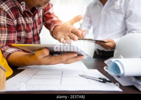 close up hand of engineer explaining project work on tablet and discussing about drawing blueprint as partner writing data on paper, architect meeting Stock Photo