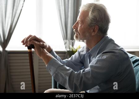 Pensive stressed middle aged disabled old man sitting on sofa. Stock Photo