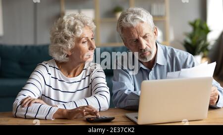 Focused middle aged retired family couple managing monthly budget. Stock Photo