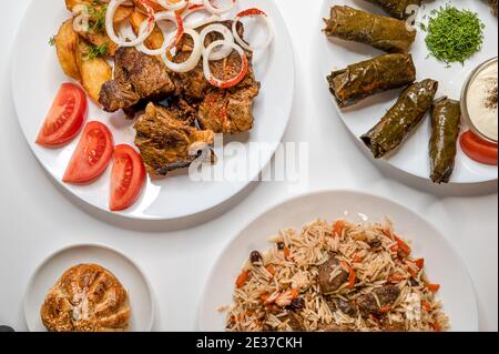 Top view of Kazan kabob, Plov, Dolma and fried chicken. Uzbek Main dishes on white plates. Stock Photo