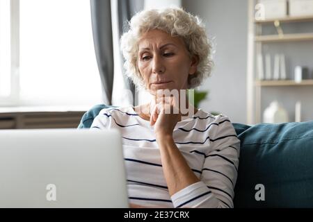 Thoughtful middle aged senior woman using computer applications. Stock Photo
