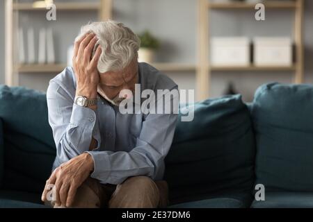 Frustrated unhappy middle aged mature man sitting on sofa. Stock Photo