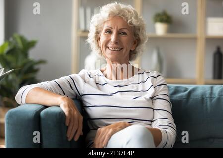 Portrait of smiling sincere mature woman relaxing on comfortable sofa. Stock Photo