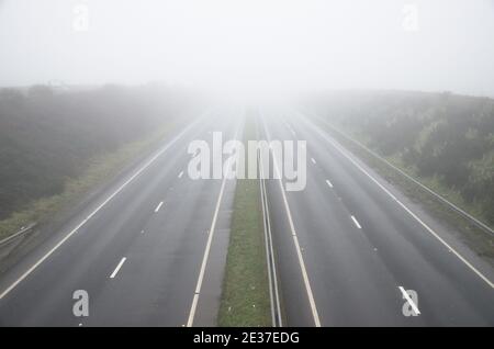 Foggy misty conditions with poor visibility make for hazardous driving conditions. Empty dual carriageway view from above. Stock Photo