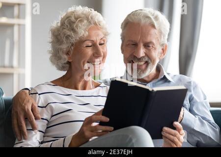 Happy bonding elderly senior retired family couple reading paper book. Stock Photo