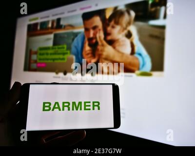 Person holding smartphone with logo of German statutory health insurance Barmer Ersatzkasse. Focus on mobile phone screen. Unmodified photo. Stock Photo