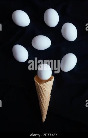 White eggs over ice cream cone. Easter eggs and ice cream cone waffle on dark background Stock Photo