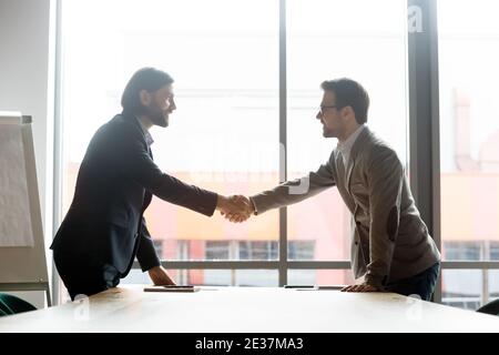 Happy two male business partners shaking hands, starting negotiations meeting. Stock Photo
