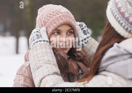 Close up portrait of caring mother adjusting hat on cue girl while enjoying walk together outdoors in winter Stock Photo