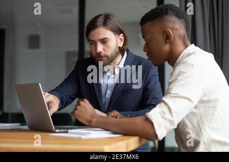 Concentrated two mixed race coworkers discussing presentation on laptop. Stock Photo