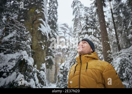 Portrait of young man in winter nature. Tourist in warm clothing against rocks in the middle forest during snowing. Adrspach, Czech Republic Stock Photo