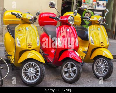 Two yellow Vespa Sprint 150 Sport and red Vespa Primavera 150 scooters stand on the street of Florence. Italian scooter brand manufactured by Piaggio. Stock Photo