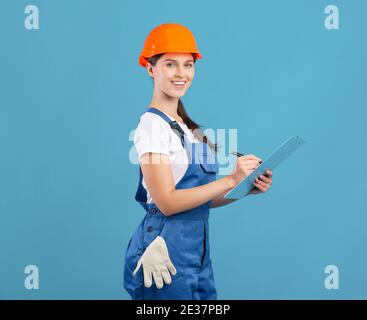 Portrait Of Happy Maintenance Worker Lady In Coverall And Hardhat With Clipboard Stock Photo