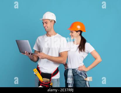 Happy young couple in hardhats using laptop, ordering materials for repair apartment Stock Photo