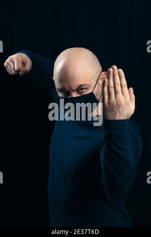 Portrait of a bald man in a black medical mask on a dark background. Threatening gestures for disease and viruses Stock Photo
