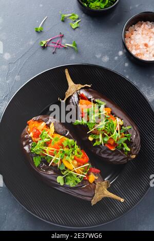 Baked stuffed eggplant with different vegetables, tomato, pepper, onion and parsley in round black plate on dark stone or concrete table background. T Stock Photo