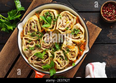 Meat dough rolls with meat or lazy dumplings in a cast-iron pan on an old rustic dark wooden background. Top view. Stock Photo