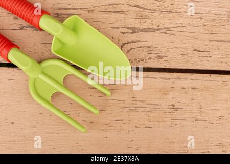 Light green garden hand tools, a shovel and a rake with orange handles, lie on painted boards. Stock Photo