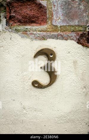 A shiny golden 3 on a crumbling plaster wall with brick beneath Stock Photo