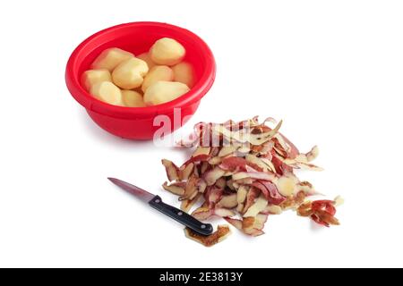 Raw peeled potatoes in red plastic cup, potato peel and kitchen knife isolated on white background Stock Photo
