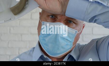 Engineer Portrait Wearing Helmet and Medical Face Mask Is Wiping His Head from Sweat Stock Photo